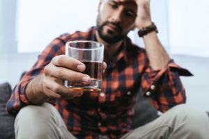 man struggling with the dangers of drinking alcohol while quitting drugs