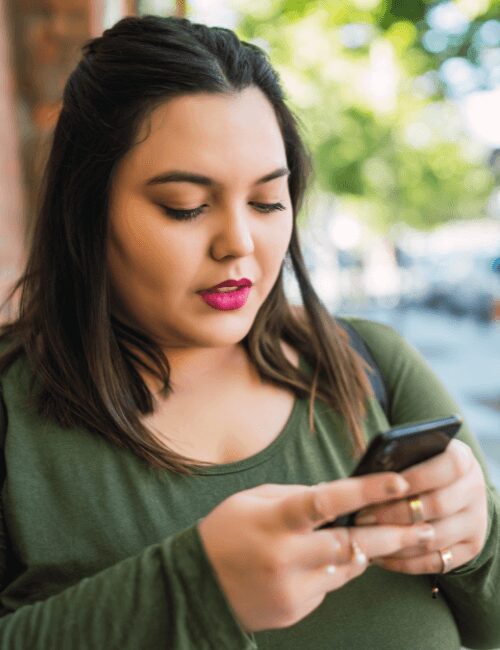 Young woman standing outdoors checking her phone for Anthem BCBS rehab coverage