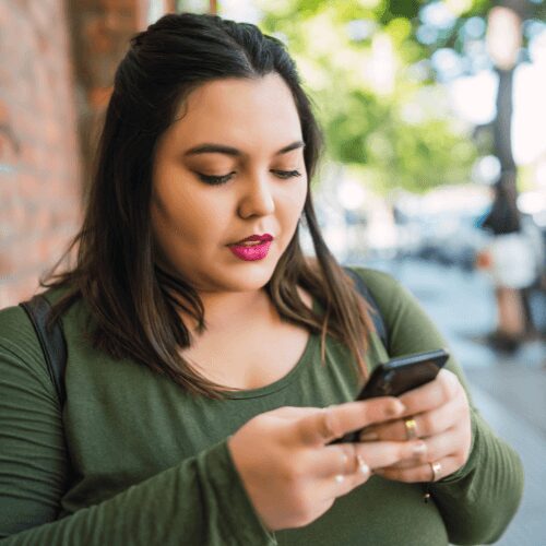 A woman standing outdoors and using her phone to check UHC addiction rehab coverage