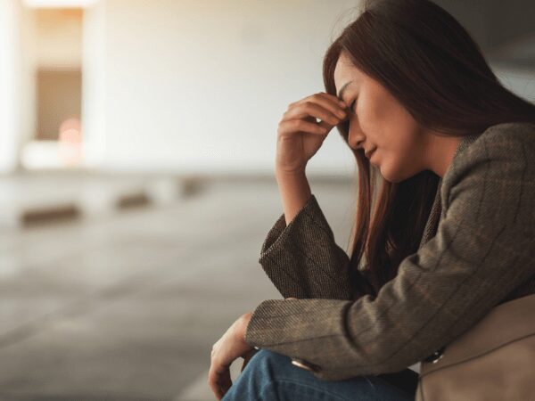 A distressed woman sitting on a curb in a parking garage in need of a PHP addiction rehab program