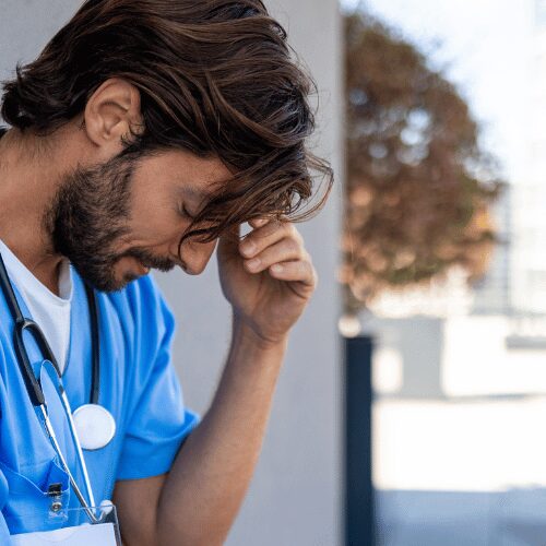 Stressed healthcare worker leaning on a wall outside the facility
