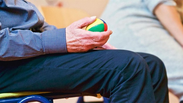 Close-up shot of an elderly man holding a multicolored ball while sitting in a chair.