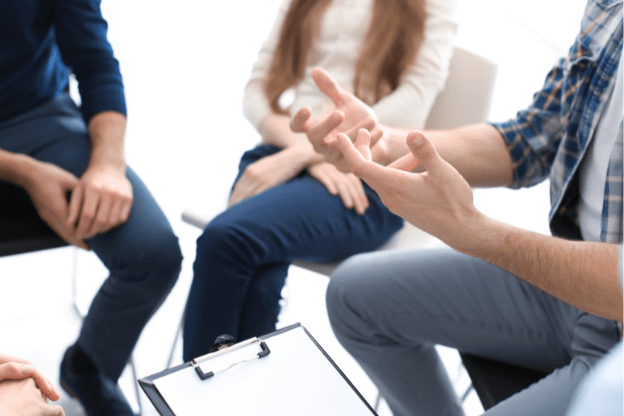 A man gesturing during a group therapy session that shows participants from the shoulders down